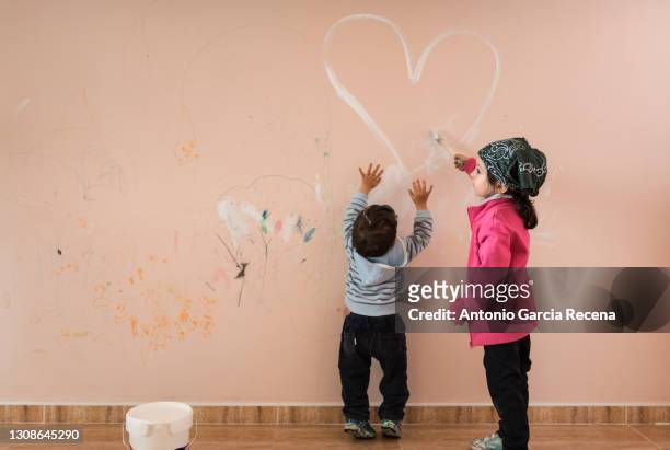 little children at home. siblings painting room wall with white paint. - baby paint stock-fotos und bilder