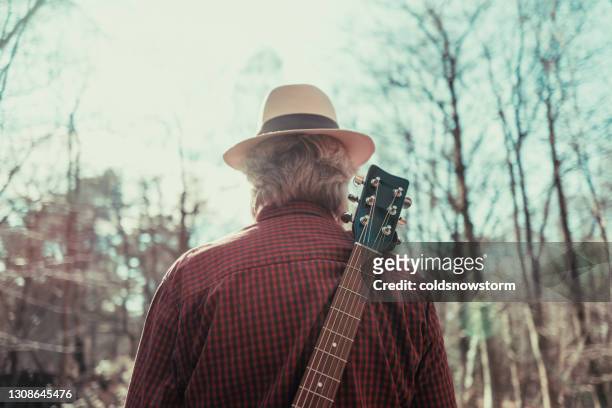 rear view of man walking on country road with guitar on his back - blues musician stock pictures, royalty-free photos & images