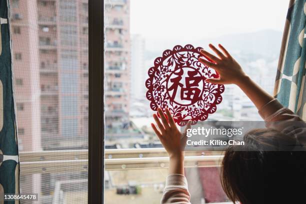 asian woman hanging a chinese new year decoration "fu" (福）at home - chinese window pattern stockfoto's en -beelden