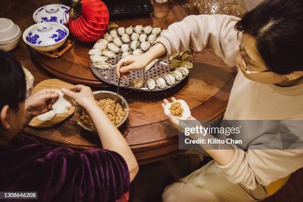 asian senior mother and daughter making chinese dumpling (jiaozi) together in the kitchen - chinese lantern festival stock pictures, royalty-free photos & images