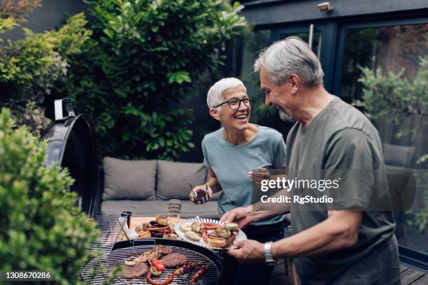 pareja mayor asando carne y disfrutando en el patio trasero - asador fotografías e imágenes de stock