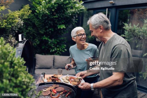 pareja mayor asando carne y disfrutando en el patio trasero - barbecue grill fotografías e imágenes de stock