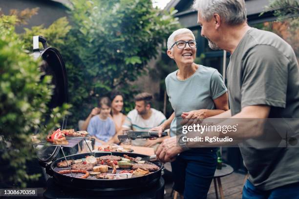 happy senior couple enjoying making barbecue for their family - family in garden imagens e fotografias de stock