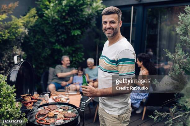 portrait of a man making barbecue for the family and enjoying beer - senior men beer stock pictures, royalty-free photos & images