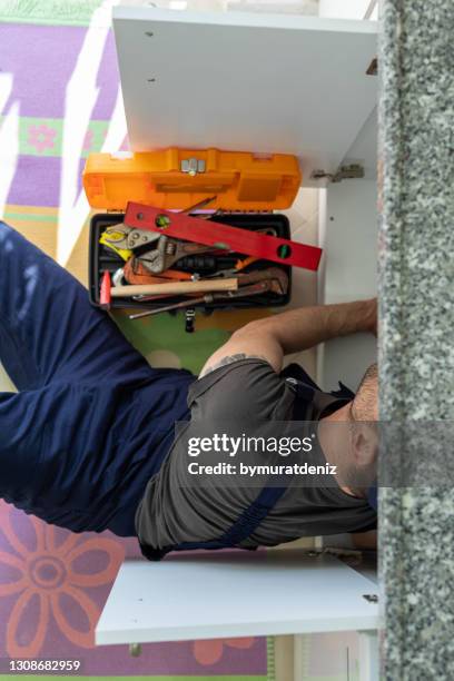 colpo di un uomo che ripara un tubo sotto il lavandino della cucina - under sink foto e immagini stock