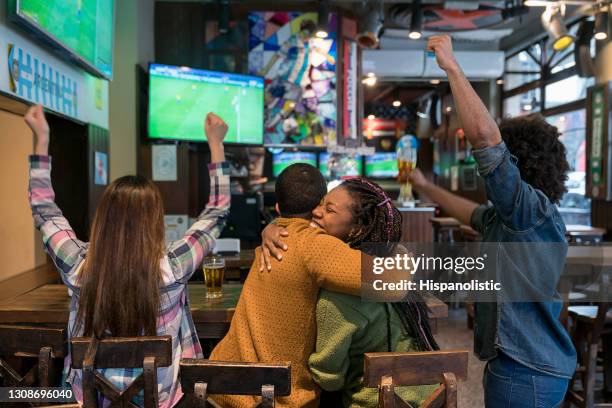 vista sul retro di diversi amici che celebrano il trionfo dell'argentina in una partita di calcio al bar abbracciandosi mentre si godono birra e snack - amici calcio foto e immagini stock