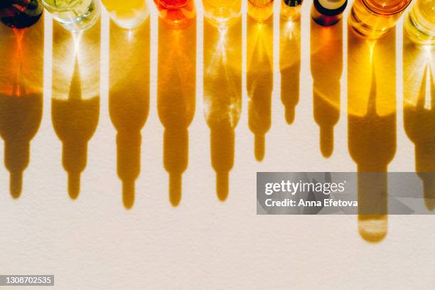 set of many different glass bottles with cosmetic liquids placed in a row on pastel beige surface. play of light creates abstract patterns from shadows and illuminating yellow reflections. trendy colors of the year 2021. flat lay style with copy space - vitamine c stockfoto's en -beelden