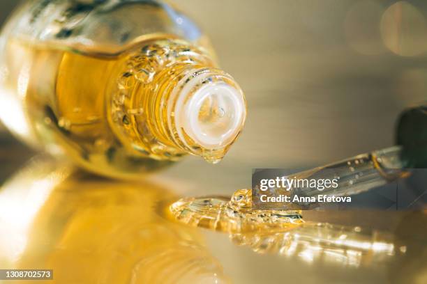 drops of bright yellow essential oil with air bubbles are dripping from glass bottle and pipette on ultimate gray surface. trendy colors of the year 2021. extreme close-up and front view - jojoba oil stock pictures, royalty-free photos & images