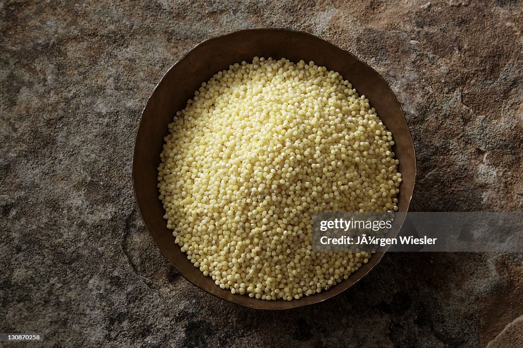 Millet (Panicum miliaceum) in a copper bowl on a stone surface