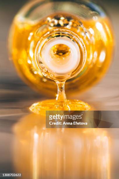 drop of bright yellow essential oil with air bubbles is dripping from glass bottle on ultimate gray surface. trendy colors of the year 2021. extreme close-up and front view - jojoba stockfoto's en -beelden