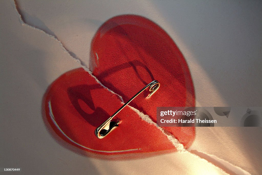 Broken red love heart repaired with a safety-pin