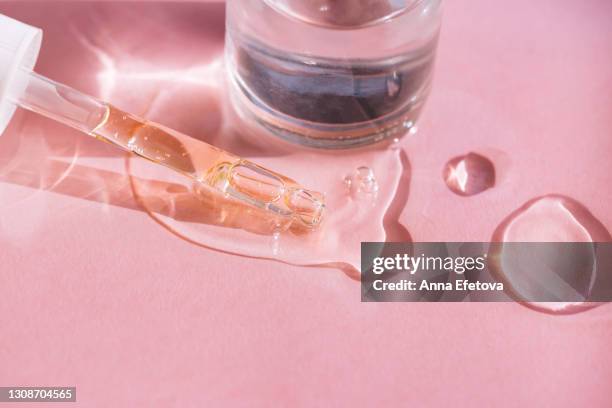 close-up of drops of facial serum or essential oil with pipette and glass bottle on pink background. trendy products of the year. health and wellness concept - ácido hialurónico imagens e fotografias de stock