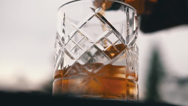 Pouring whiskey into glass with ice cube