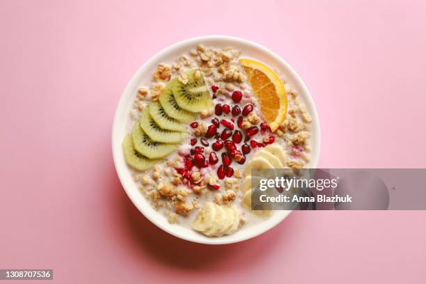 breakfast cereal meal granola with milk, pomegranate, kiwi and orange in bowl and spoon over pink background - cereal bowl stockfoto's en -beelden