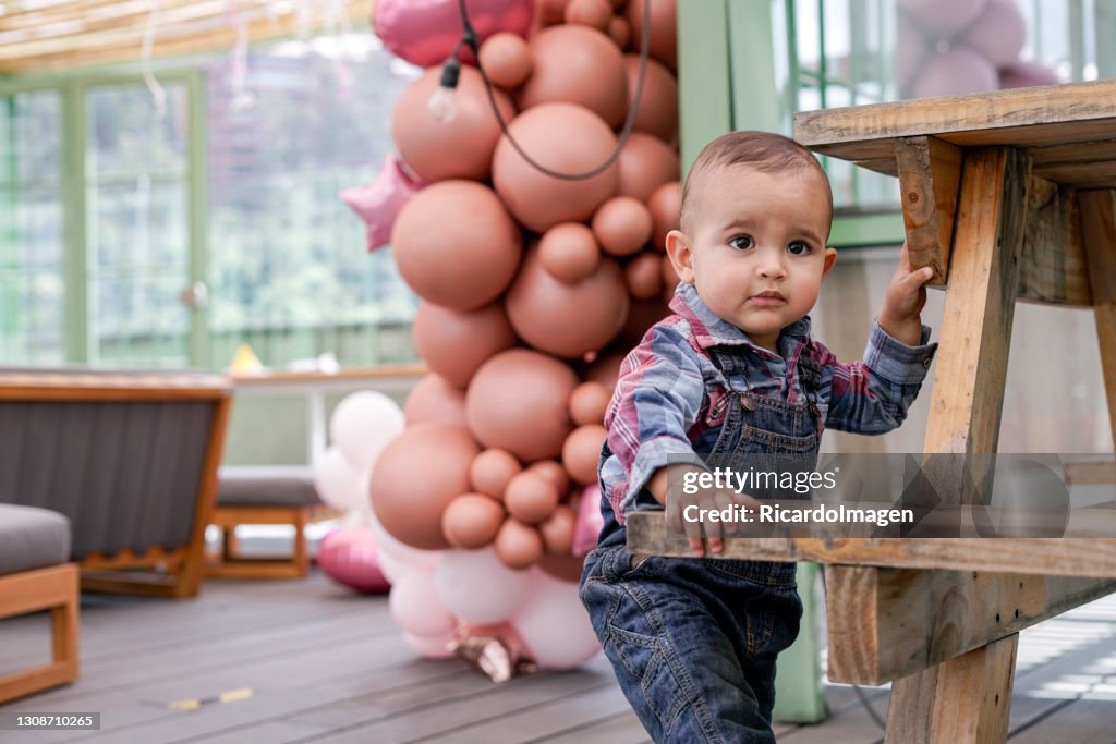 Barn av latino etnicitet firar födelsedag. Han tittar på kameran och bakom dekorationsballongerna till festen.