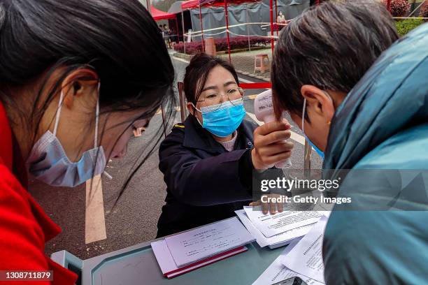 Officials test residents body temperatures as the line up to receive the COVID-19 vaccine at the Community hospital on March 23, 2021 in Wuhan, Hubei...