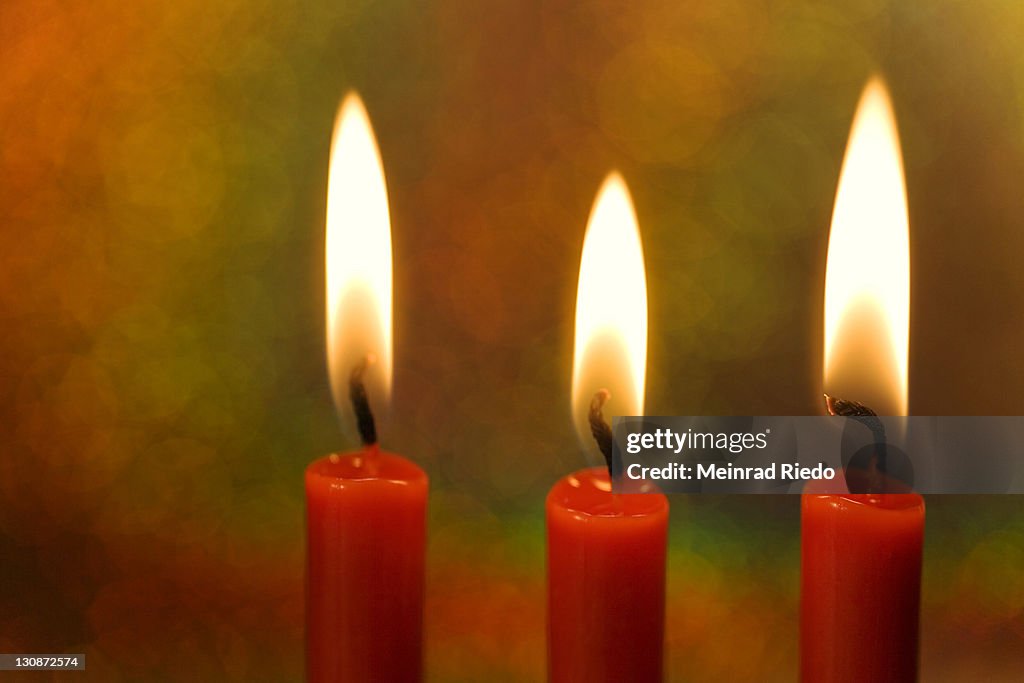 Three burning candles in front of a colourful background