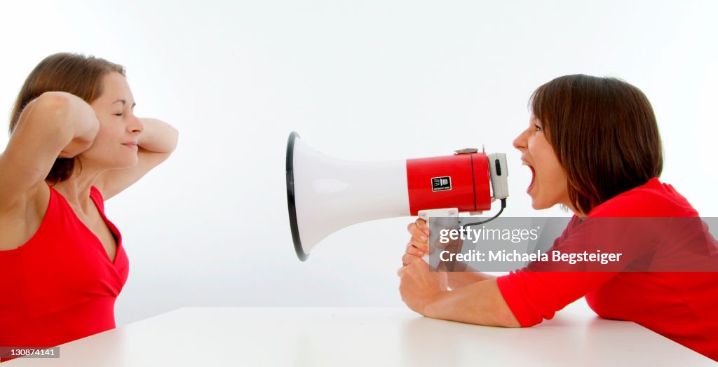 Woman screaming in megaphone, other woman keeps shut ears