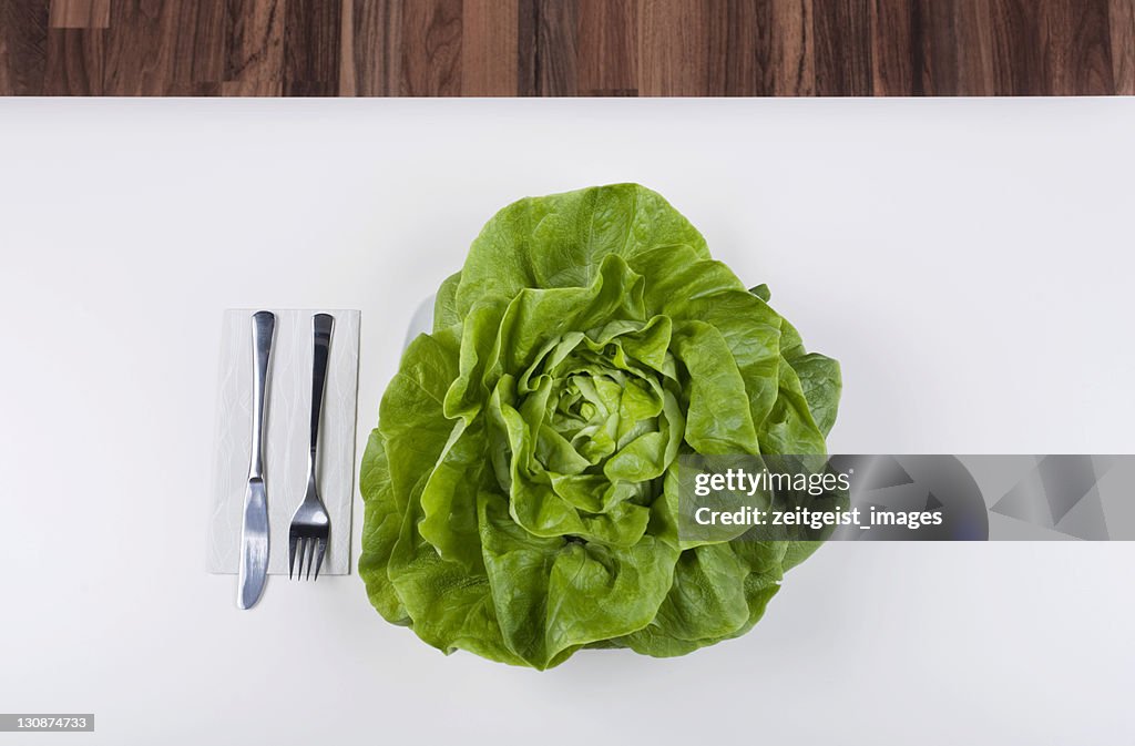 Head of lettuce on a plate, cutlery beside it