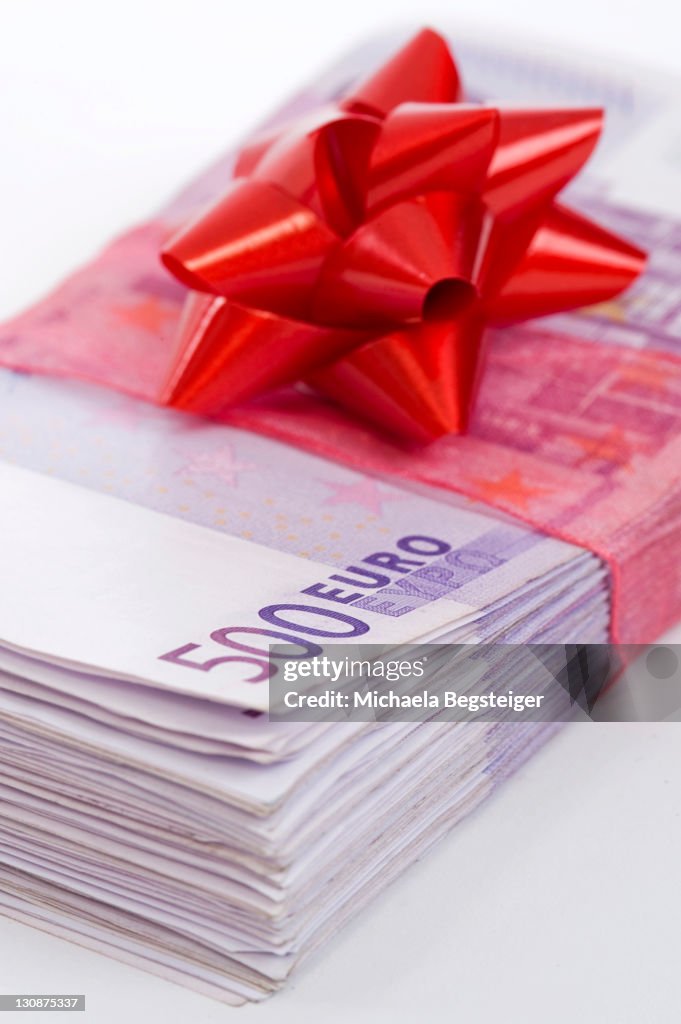 Wad of 500 Euro banknotes with red bow, symbolic of money gift