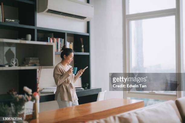 asiatische chinesische schöne frau genießen ihren nachmittagstee im wohnzimmer blick nach draußen fenster entspannen auf dem tisch lehnen - air conditioning stock-fotos und bilder