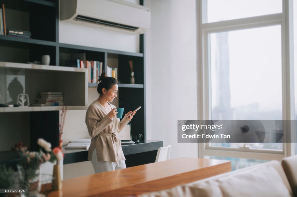 Asiática china hermosa mujer disfrutando de su té de la tarde en la sala de estar mirando fuera de la ventana relajarse apoyado en la mesa