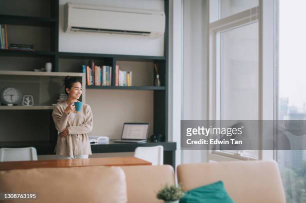 aziatische chinese mooie vrouw die van haar middagthee geniet bij woonkamer die buitenvenster kijkt ontspant leunend op lijst - airco stockfoto's en -beelden