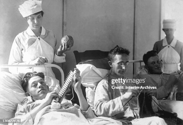 View of bed-ridden, wounded soldiers knitting under the watchful eye of nurses at Walter Reed Hospital, in Washington, DC, 1918.