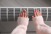 Woman warming hands near electric heater at home,  top view