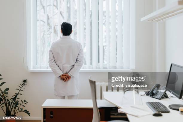 docteur asiatique mâle contemplant dans son bureau - hands behind back stock photos et images de collection