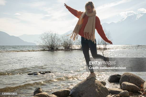 joven salta de roca en roca a orillas del lago - equilibrio fotografías e imágenes de stock