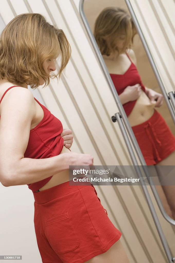 Thin, young woman standing in front of a mirror, checking the size of her belly