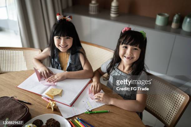 portrait of sisters at home doing origami - folding origami stock pictures, royalty-free photos & images