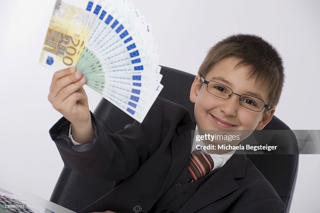 Boy dressed as a businessman holding a fan of banknotes