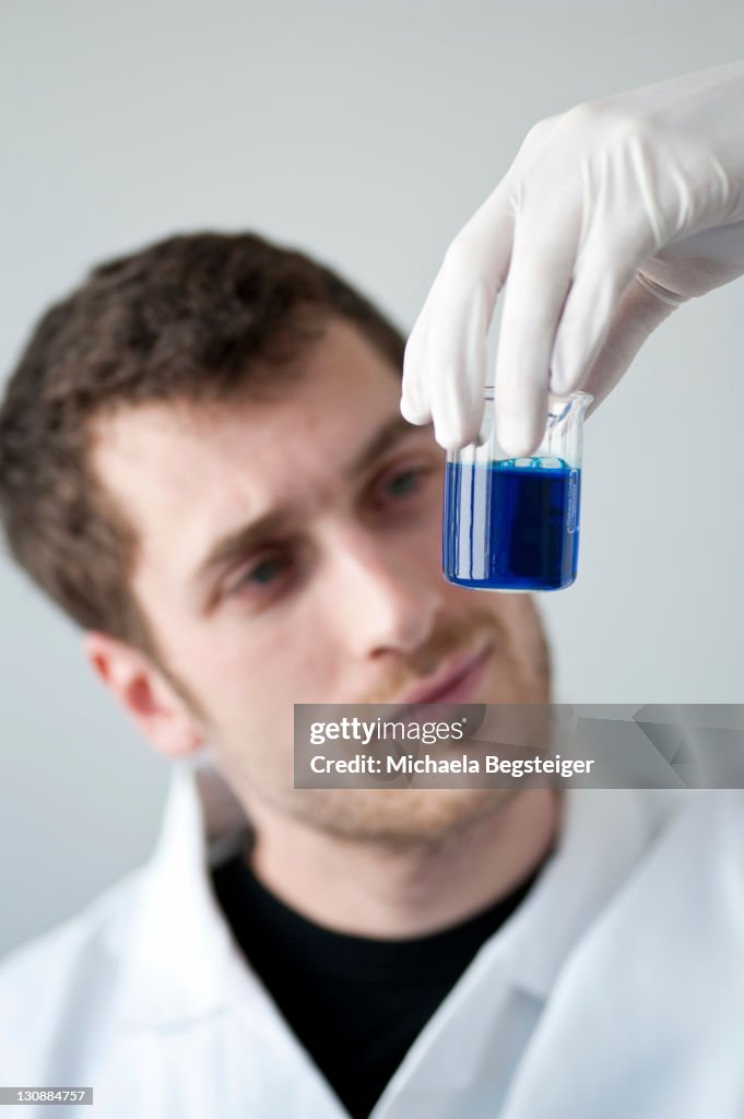 Chemist holding a measuring cup filled with a blue liquid