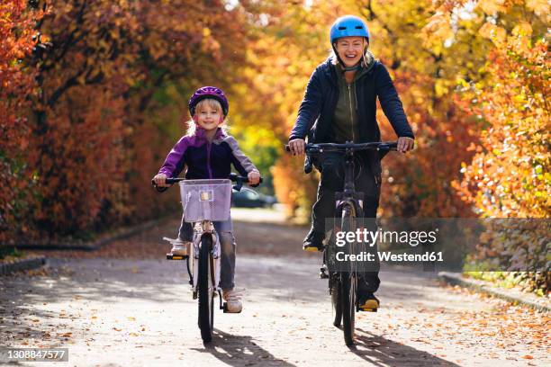 happy mother and daughter cycling on road in park during autumn - finland happy stock pictures, royalty-free photos & images