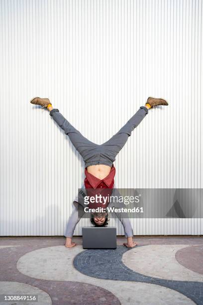 businessman looking at laptop while doing handstand against wall - équilibre sur les mains photos et images de collection