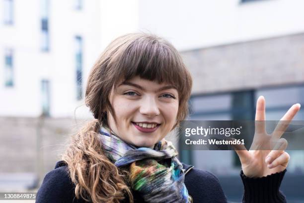 smiling woman gesturing hand sign while standing outdoors - three fingers stock pictures, royalty-free photos & images