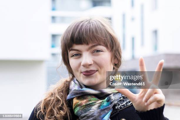 young woman smiling while gesturing hand sign standing outdoors - three objects stock pictures, royalty-free photos & images