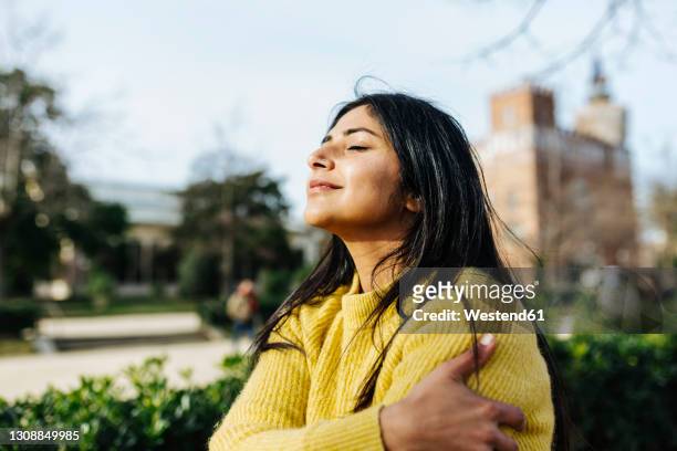 smiling woman hugging self against sky in public park - low key stock pictures, royalty-free photos & images