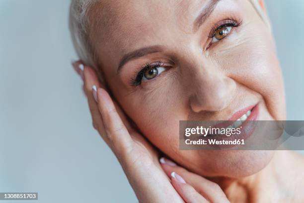 close-up of woman smiling while standing against gray background - donna 60 anni foto e immagini stock