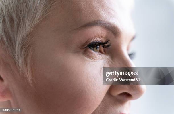 close-up of senior woman looking away against gray background - close up eye side stock pictures, royalty-free photos & images