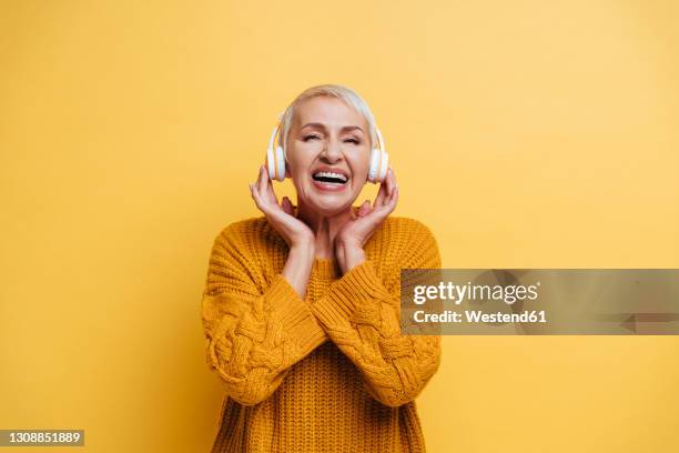 smiling woman wearing headphones standing against yellow background - listening to music old stock pictures, royalty-free photos & images