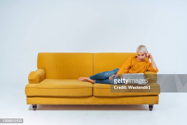 senior woman using laptop while sitting on sofa against gray background - senior woman studio ストックフォトと画像