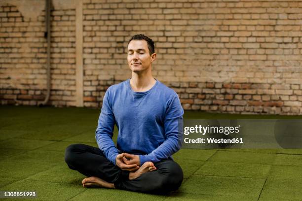 male athlete with cross legged meditating against brick wall in health club - athletic club - fotografias e filmes do acervo