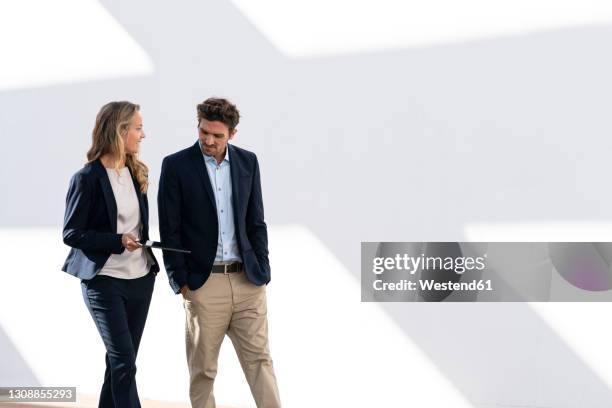 businesswoman with digital tablet having discussion while walking against white wall - two people walking stock pictures, royalty-free photos & images