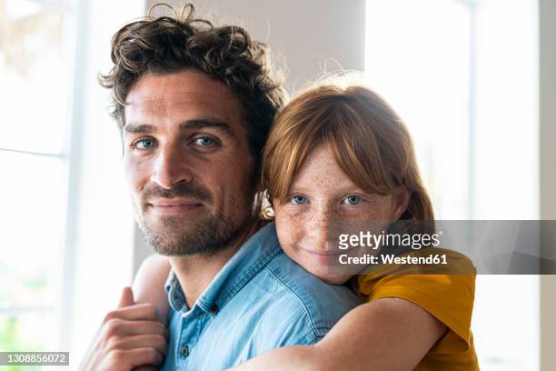 smiling redhead daughter with blue eyes cuddling father in living room - daughter stock-fotos und bilder