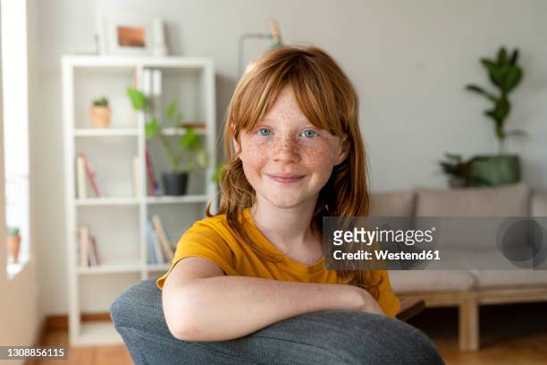 smiling redhead girl with blue eyes sitting on chair at home - 8歳から9歳 ストックフォトと画像