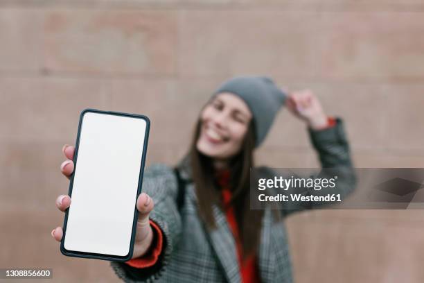 woman showing blank smart phone screen against wall - mostrare foto e immagini stock
