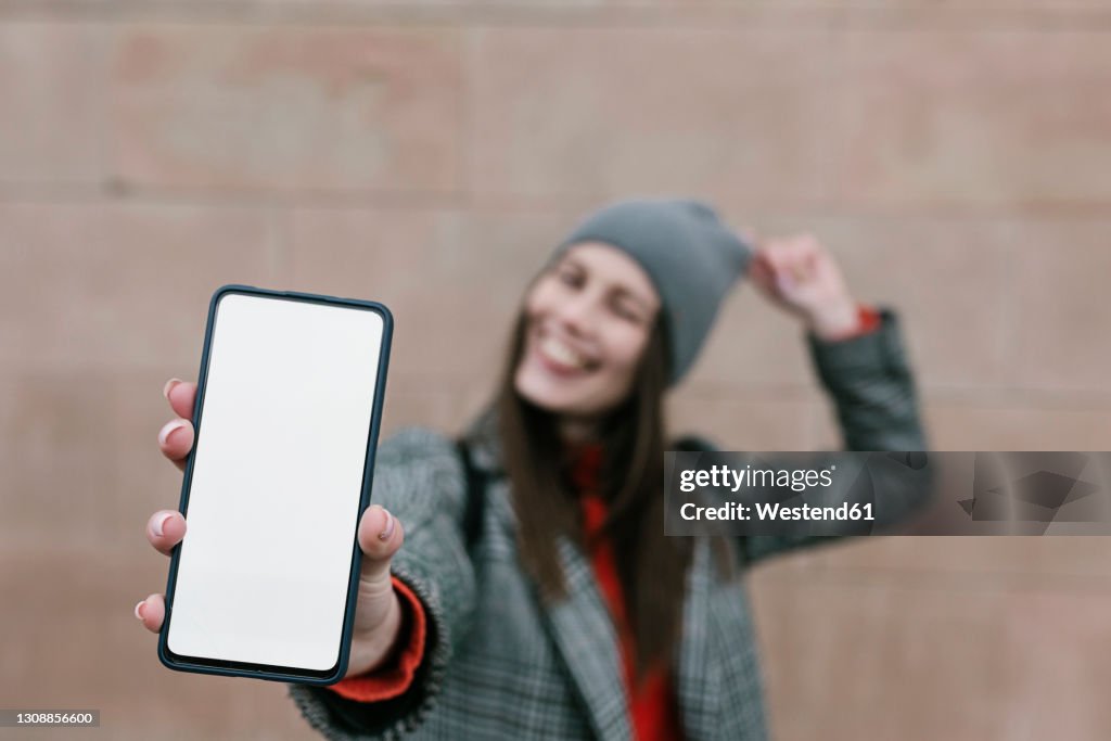 Woman showing blank smart phone screen against wall